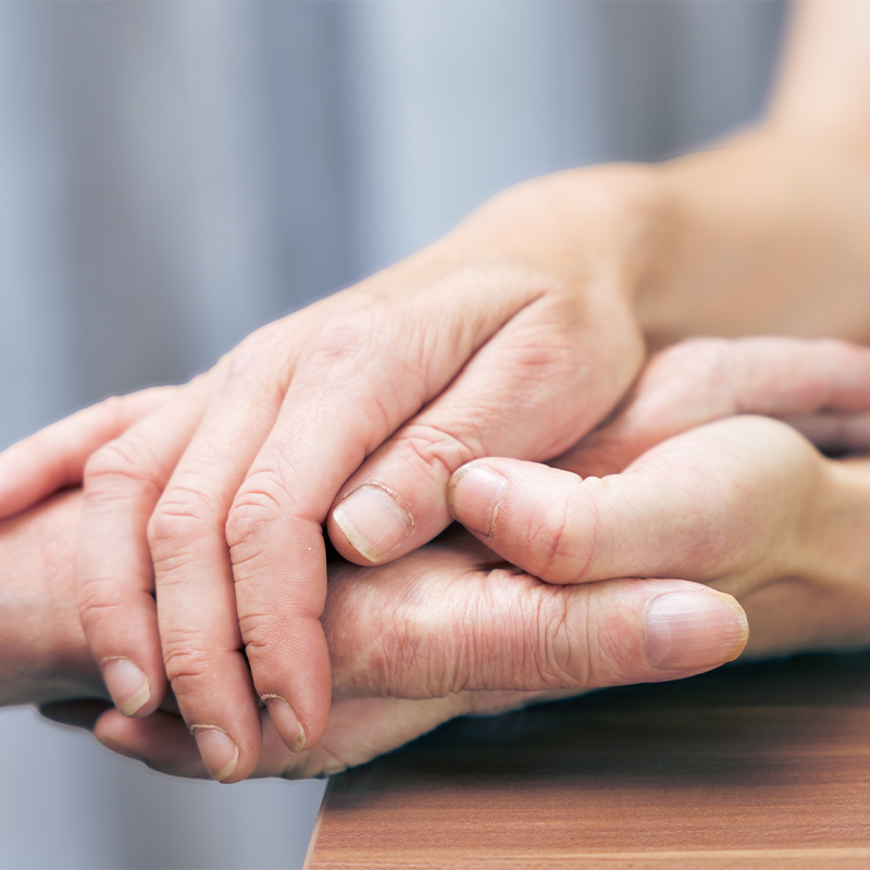 Jüngere Hand hält sanft die ältere Hand auf einem Tisch und vermittelt Fürsorge und Unterstützung.
